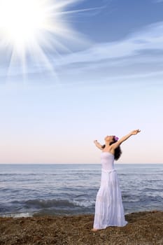 The woman in a white sundress on seacoast with open hands. Sun light