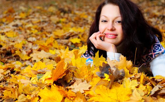 The attractive woman in autumn forest. Lies on yellow leaf