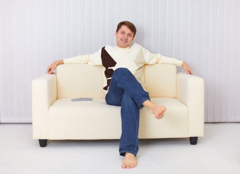 The happy guy sits on a sofa and watches TV