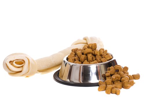 A metal bowl filled with dry dog food along with a large rawhide bone, isolated against a white background