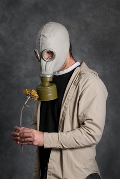 Concept image of death featuring a young man wearing a gas mask and holding a wilted flower