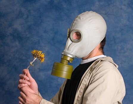 Concept image of death featuring a young man wearing a gas mask and holding a wilted flower