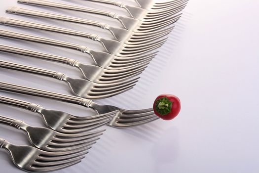 Forks and hot papper lie abreast on a white rough kitchen table.