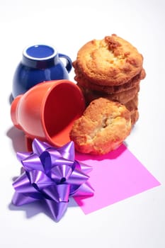 Sweet cookies with cups for coffee, a celebratory bow and a label of red colour in the foreground.