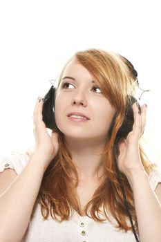 young redhead woman is daydreaming while listening to music with headphones on white background