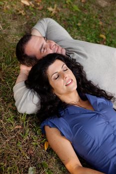 A couple laying on grass in a park daydreaming.  Focus on the womans eyes