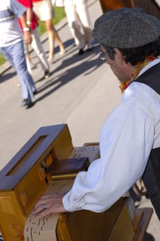 A man plays his barrel organ in the street as pedestrians hurry by.