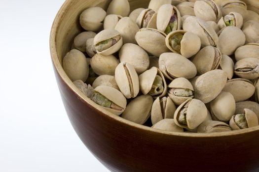 a wooden bowl of salted and roasted pistachio nuts, white copy space