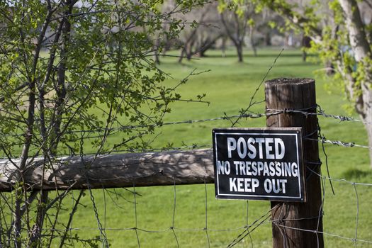 no trespassing - keep out sign on a fence surrounding green meadow or golf course