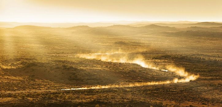 two cars leave plumes of dust as they go through the desert at sunset