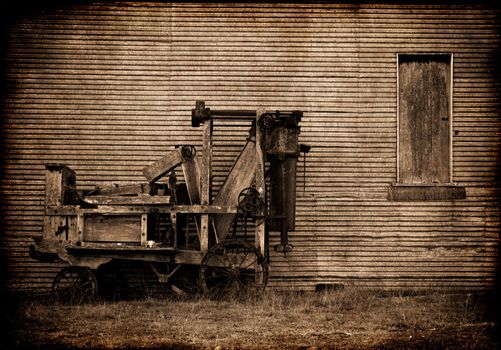 grungy image of old baler in front of a barn on the farm in sepia 