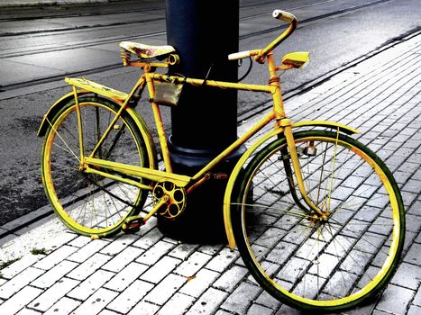 Single, yellow bicycle stand in the pavement and   propped against the lamp-post. 