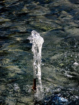 White short fountain column with water in background. 