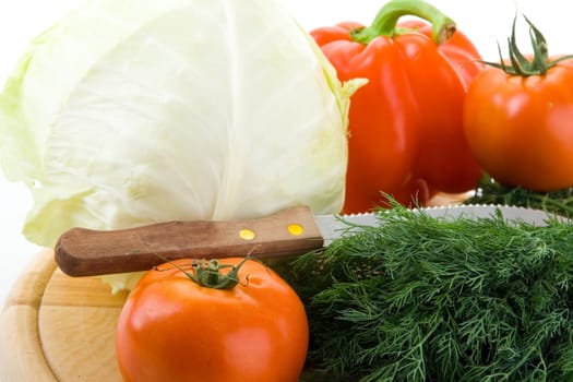 Cabbage, fennel, tomatoes and bell peppers on a wooden cutting board on a white background