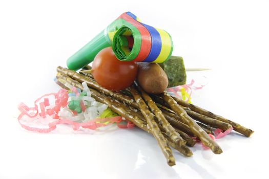 Salty brown tasty pretzels and party blower with cocktail stick containing hot dog, gherkin and tomato with streamers on a reflective white background