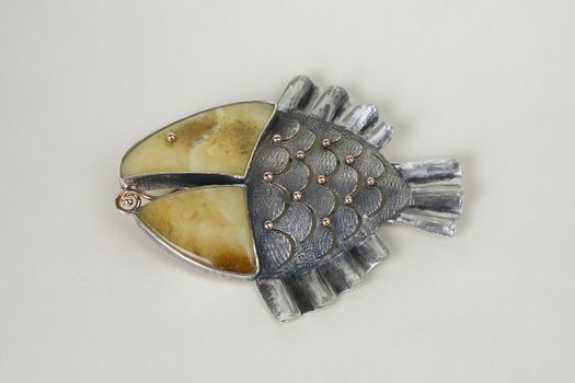 Brooch, made from gold, silver and amber on the light background.
