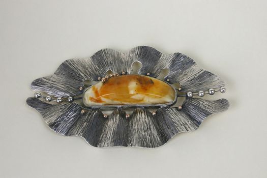 Brooch, made from gold, silver and amber on the light background.
