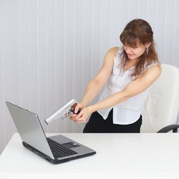 The young woman shoots at the laptop from a pistol