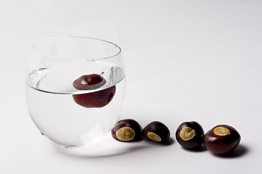 Glass cup filled with water containing one chest nut, four chest nut are on the side waiting to get their turn to dip