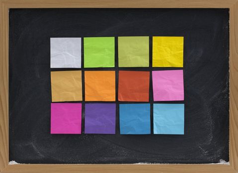 a dozen of blank, colorful sticky notes on a blackboard with white chalk smudges