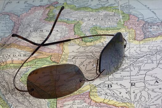 travel concept - sun glasses over vintage, warn out,  ninety year old map of South America (New International Atlas of the World, 1926 edition) with Braziil, Peru, Ecuador, Colombia, Venezuela and Guiana, focus on Amazonia