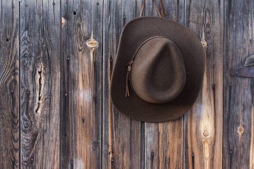 brown wool felt cowboy hat with leather headband hanging on weathered wooden wall of old barn