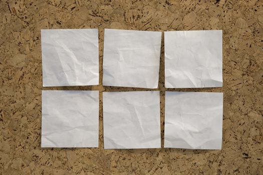 six blank crumpled white sticky notes on a cork bulletin board
