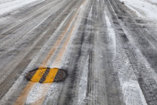 street asphalt pavement covered by snow and ice, double yellow line across manhole cover