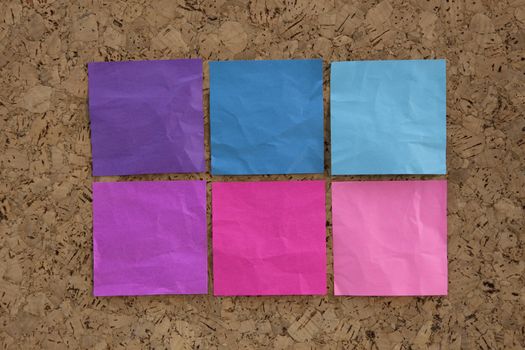 six blank crumpled sticky notes in blue, pink, magenta colors on a cork bulletin board