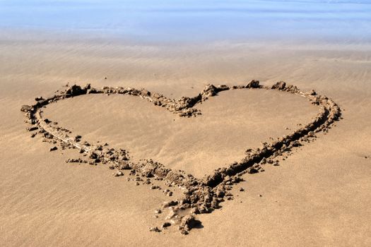 a romantic love heart inscribed on the beach with waves in the background on a hot sunny day
