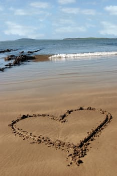 a romantic love heart inscribed on the beach with waves in the background on a hot sunny day
