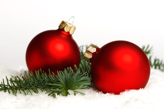 Two red christmas balls, fir branch on snow, isolated on white background