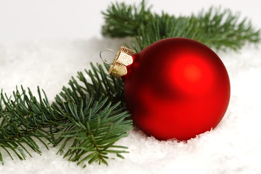 A red christmas ball, fir branch on snow, isolated on white background