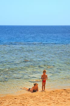 ma and son playing on beach on background blue sky