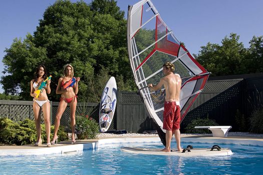 Windsurfer in a pool with two women in bikini with water gun