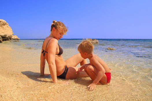 ma and son playing on beach on background blue sky 