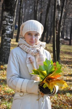 Young woman with a bouquet of maple leaves in an autumn wood