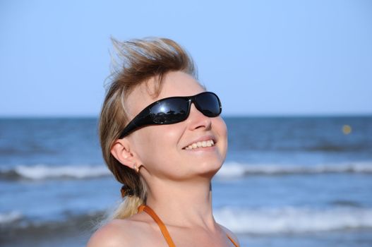 young woman wearing a sunglasses reflecting the beach. sun and an umbrella