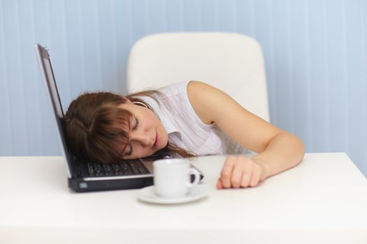 The young woman sleeps on the laptop keyboard on a workplace