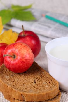 Black bread with milk and red apples against the newspaper with a pencil removed close up