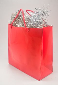 Shiny red gift bag filled with silver tinsel against plain background