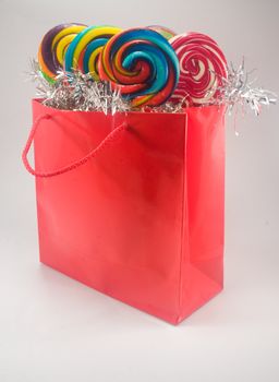 Shiny red gift bag filled with candy against plain background