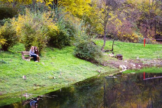 two cute women outdoors in autumn sitting on bench