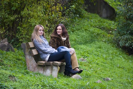 two cute women outdoors in autumn sitting on bench
