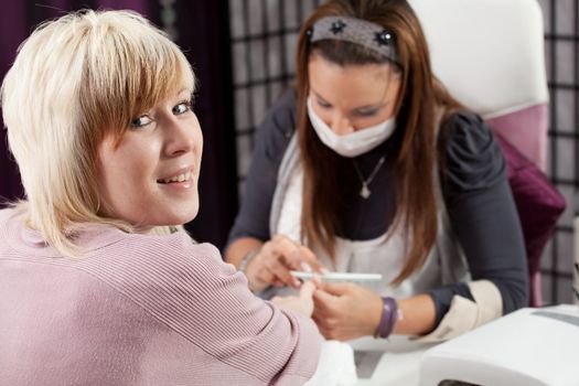 Happy nail studio client and beautician on background working on nails