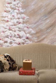 Two Christmas gifts lying on a sofa with a hand painted Christmas tree in the background