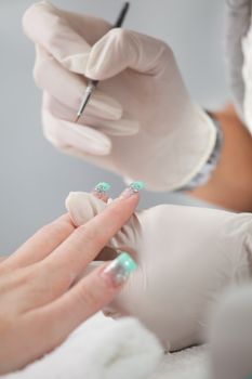 Beautician adding sparkles to fingernails. Close-up shot
