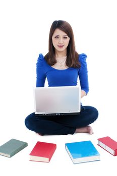 Portrait of a cute female student using laptop and books spread around over white background.