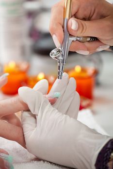 Beautician using airbrush to paint fingernails. Close-up shot