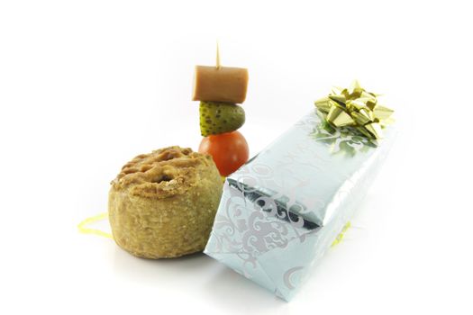 Small pork pie with a silver shiny gift and cocktail stick containing hot dog sausage, gherkin and tomato on a reflective white background